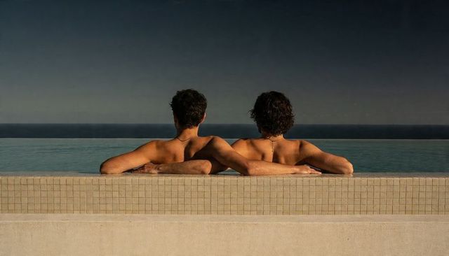 Two men relaxing in infinity pool overlooking calm ocean horizon, back view