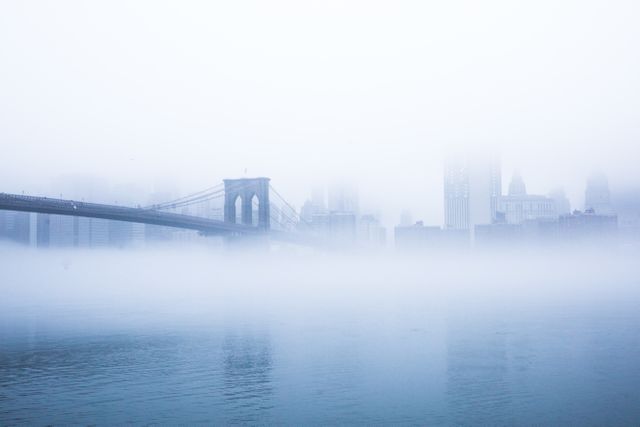 Brooklyn Bridge and Manhattan skyline shrouded in morning fog create a tranquil, dreamlike urban scene. Perfect for backgrounds, travel blogs, promotional materials for New York City, or desktop wallpapers highlighting iconic city landmarks.