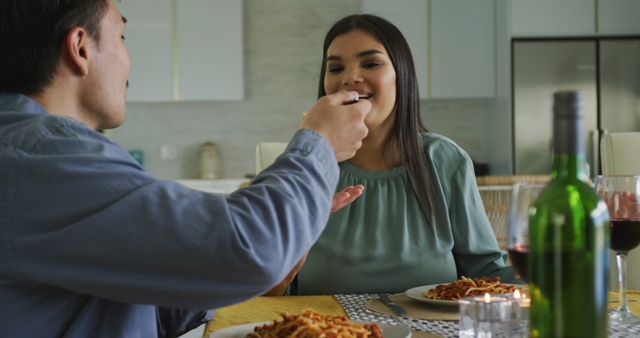 Image of happy biracial man feeding his female partner with spaghetti. lifestyle and spending time together concept.