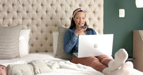 Mother Balancing Work and Family with Laptop and Smartphone on Bed