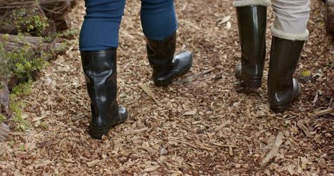 Diverse women walking on woodchip garden path wearing tall rubber boots and wellies
