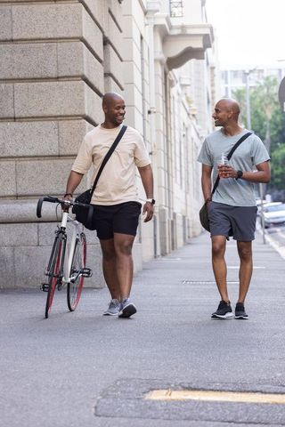 African american friends walking with bicycle and iced drink on city sidewalk casual urban stroll