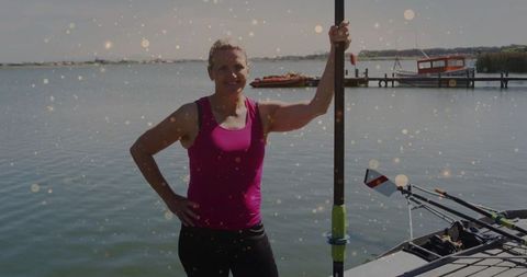 Woman standing with rowing oar by dock on serene lake