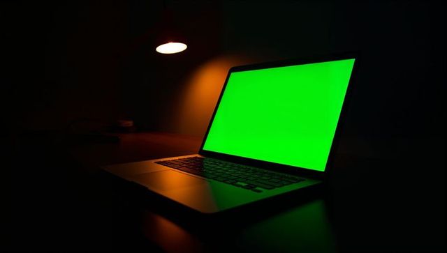 Slim laptop showing green chroma screen on dark desk under warm lamp for mockup editing