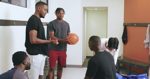 Basketball teammates discussing strategy holding ball and packing bags in locker room