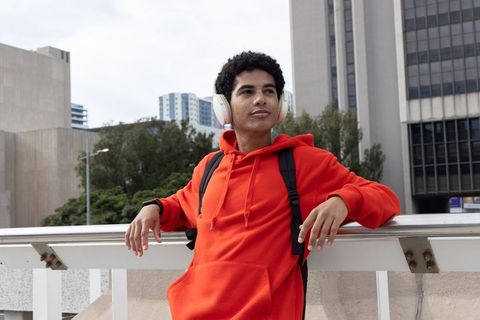 Teen male wearing red hoodie and headphones leaning on urban walkway