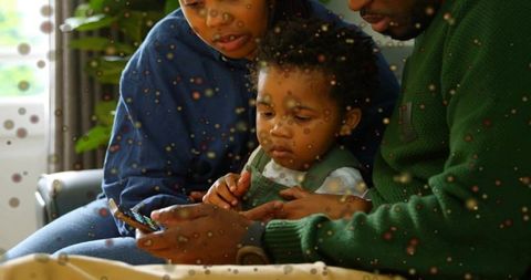 Parents guiding toddler on smartphone while sitting on couch through dotted glass pane