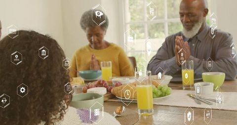 Multigenerational family praying at breakfast table with fresh juice, croissant, grapes