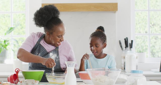 Energetic scene featuring an African American grandmother and her granddaughter baking and dancing joyfully in a home kitchen. This can be used to represent family bonds, multi-generational relationships, cooking at home, happiness, and domestic life. Ideal for advertisements, blog posts about family activities, healthy family practices, or home cooking recipes. Excellent choice for illustrating concepts of love, joy, and togetherness in family life.