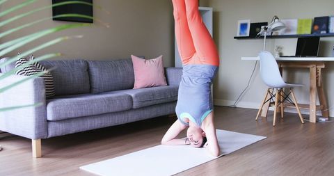 Woman practicing headstand yoga pose in cozy living room