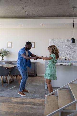 African american couple dancing playfully in modern open-plan kitchen with marble island