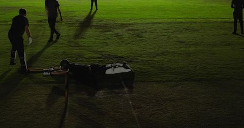 Diving batsman sliding along crease under floodlights during night cricket match