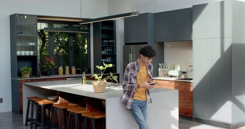 Man Relaxing in Modern Kitchen with Smartphone and Indoor Plant