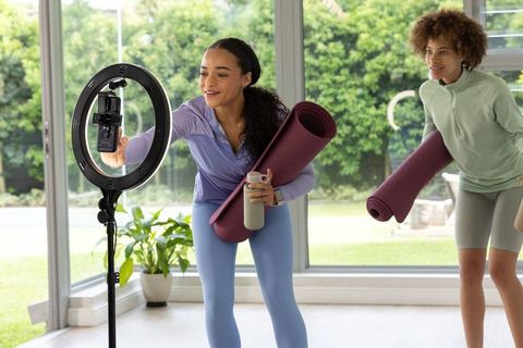 African american women recording yoga adjusting smartphone on ring light holding mats