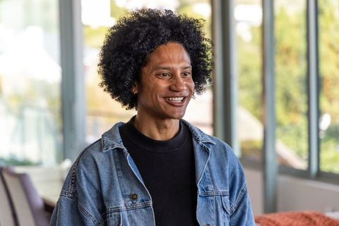 African american man smiling in bright lounge wearing denim jacket and black sweater