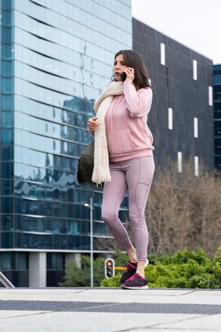 Woman talking on phone wearing pink activewear and scarf in urban office plaza morning