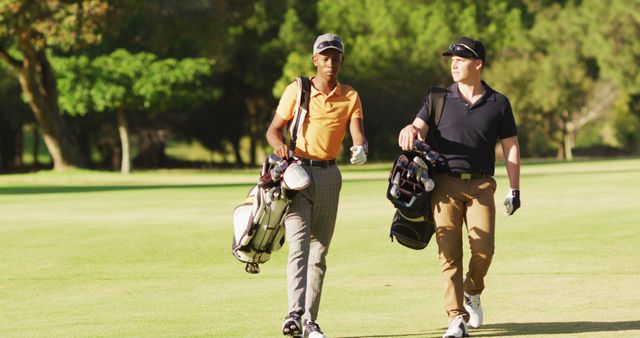 Two friends are enjoying a sunny day while walking on a golf course, carrying their golf clubs. This image can be used in advertisements for outdoor sports, promotions for golfing communities, or articles about friendship and healthy lifestyles.