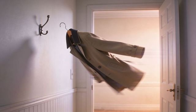 Beige trench coat floating on hanger moving through doorway with motion blur, home