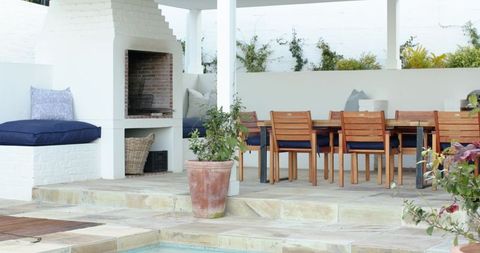 Poolside pergola dining area featuring brick fireplace and wooden table with navy cushions