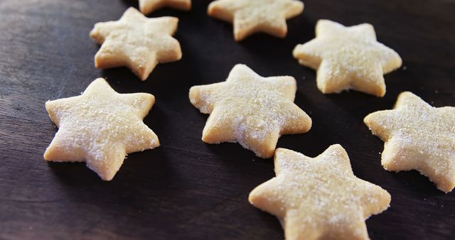 Star-shaped cookies are sprinkled with sugar on a dark wooden surface, creating a delightful treat. Their shape and dusting make them perfect for festive occasions or as a sweet snack.