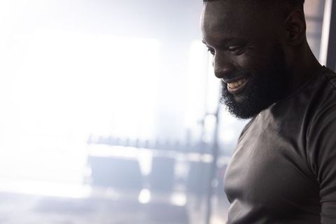 Smiling African American Man Training in Gym Wearing Fitted Tee Near Dumbbell Rack