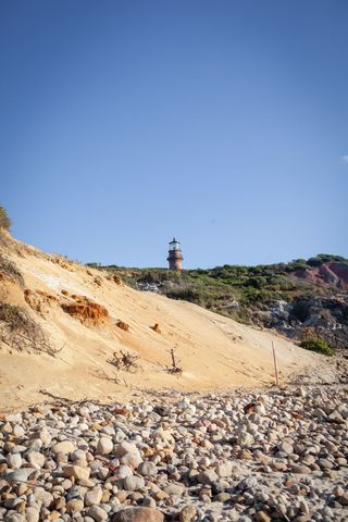 Historic lighthouse overlooks rocky beach shoreline on clear day