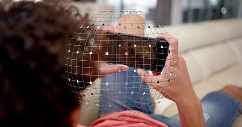 Reclining man using smartphone with spherical AR data grid overlay on living room sofa