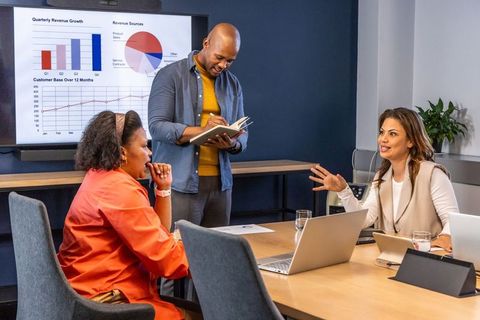 Multiracial team discussing quarterly growth charts with laptops in modern office meeting