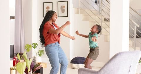 African american mother and daughter dancing in bright modern living room, joyful movement