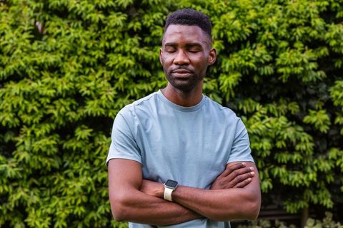 African american man standing with arms crossed in garden wearing smartwatch, serene