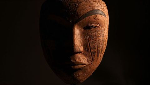Carved wooden mask with painted brows and geometric motifs in dramatic low light