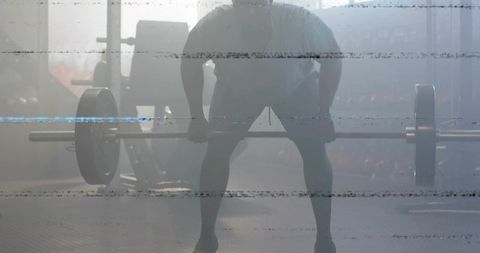 Backlit male deadlift silhouette gripping barbell in hazy gym with film-like scratches