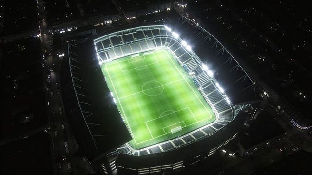 Aerial night floodlit soccer stadium glowing with vibrant green pitch
