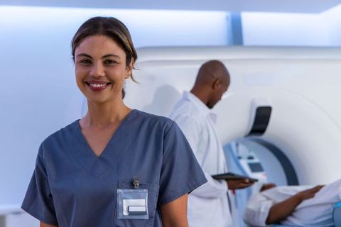 Smiling african american radiology nurse in gray scrubs showing badge with mri team