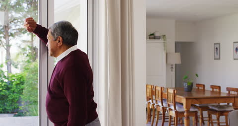 Elderly Man Thoughtfully Gazing Out Home Window During Daytime