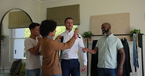 Groom receiving help with tie from groomsmen before wedding