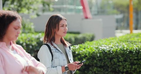 African women using smartphone in urban plaza wearing denim jacket and smartwatch