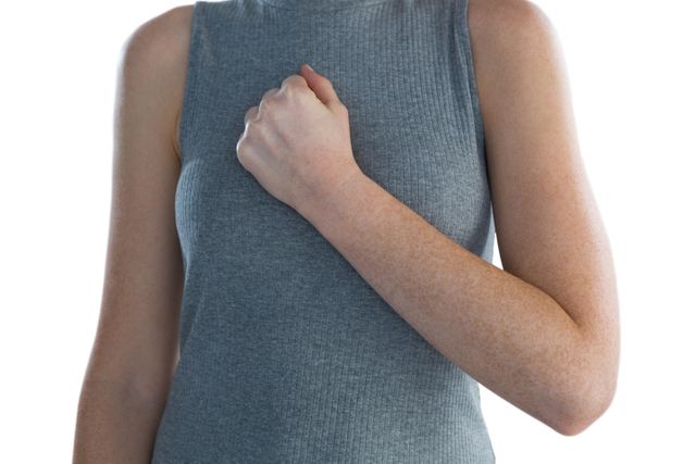 This image depicts a businesswoman standing with her hand on her chest, wearing a grey sleeveless top. The white background emphasizes the professional and confident gesture. Ideal for use in business presentations, corporate websites, or articles about professional conduct and confidence.