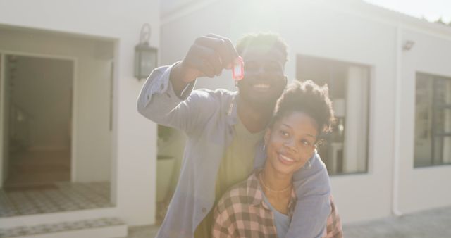 Image of happy african american couple embracing and showing keys to new house. love, relationship, and starting new life together.