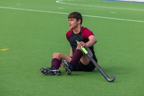 Teen Boy Resting on Turf with Hockey Stick in Hand Outdoor