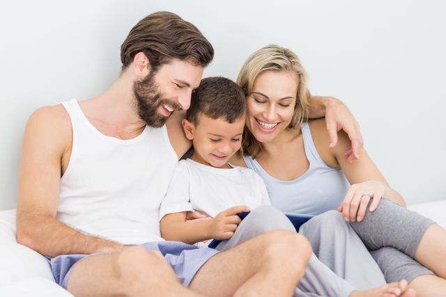 Parents and son sitting on bed and using digital tablet at home