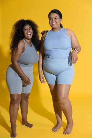 Laughing and posing plus-size women wearing ribbed activewear on vibrant yellow backdrop