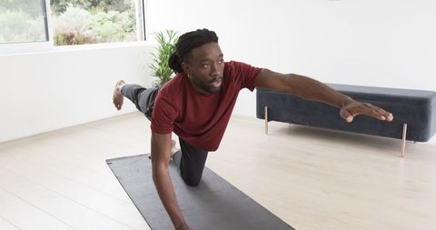 African American man practicing bird dog balance exercise on yoga mat in living room