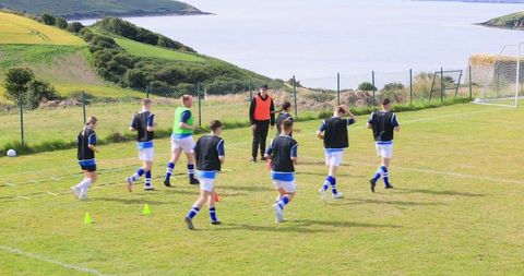 Teen Soccer Players Drilling on Coastal Pitch with Coach and Sea View
