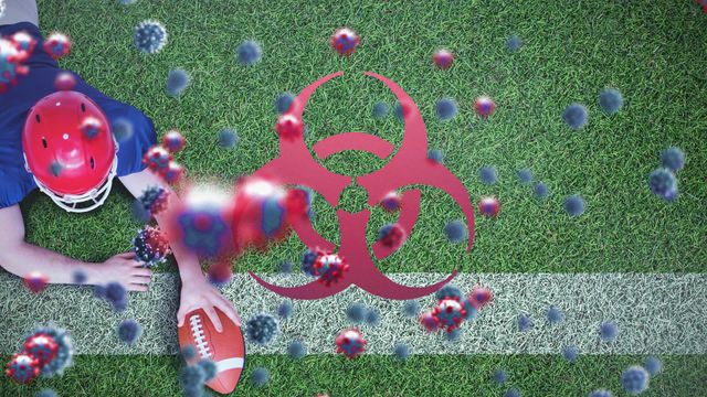 Animated COVID-19 particles surround football player lying on the ground with football on a vibrant green turf covered?. Biohazard symbol indicates potential health risks. Useful in discussions and educative material about health safety during sports events, pandemic implications in sports, and precautionary measures. Can be used for websites, presentations, or educational blogs focusing on health and sports during COVID-19 times.