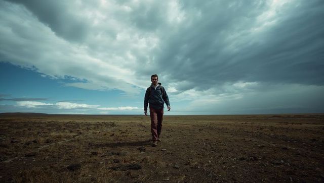 Solitary hiker trekking across barren plain under dramatic storm clouds, wilderness journey