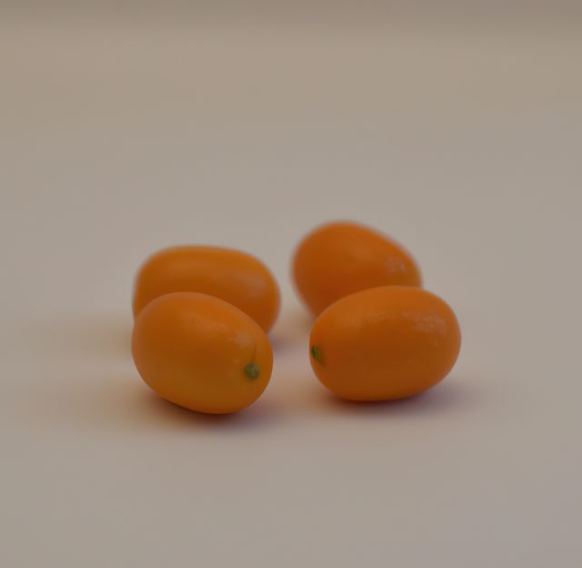 Four ripe kumquats placed on a clean white surface, ideal for use in promoting healthy eating and nutrition. Useful in brochures, websites, or blogs related to organic food, recipes, and citrus fruits.
