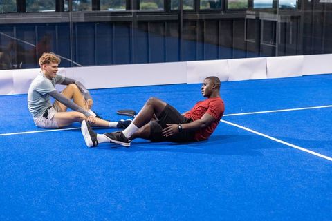 Diverse friends resting on vibrant blue padel court after match, teamwork and fitness