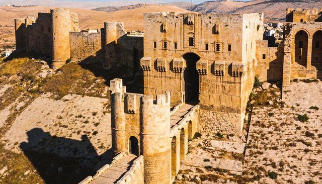 Hilltop medieval citadel gate with twin round towers, raised causeway and crenellated walls