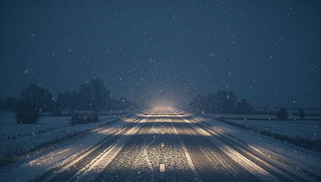 Stretching snowy highway at night glowing with headlights and tire tracks in falling snow